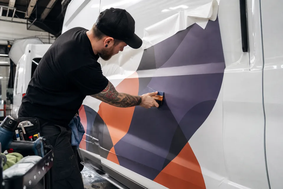 Installer squeegeeing printed vinyl onto the side of a white van